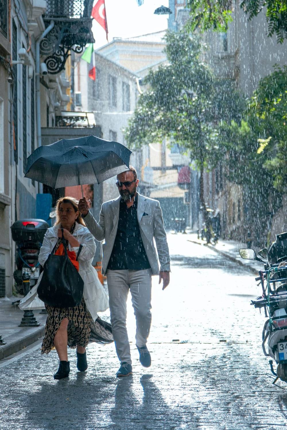 Two people walking under an umbrella down a rain-soaked alley
