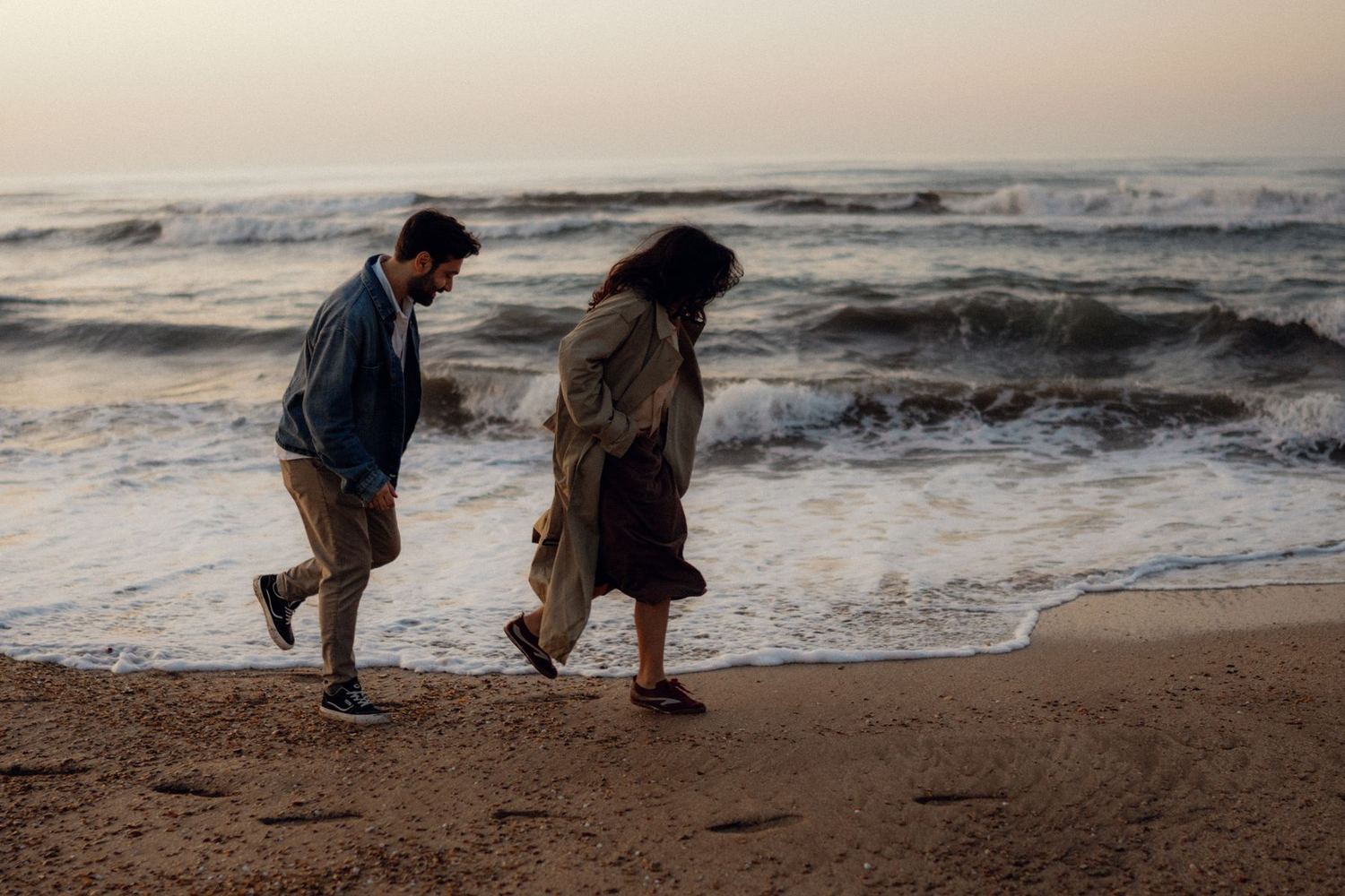 A couple walking along the shoreline with waves behind them