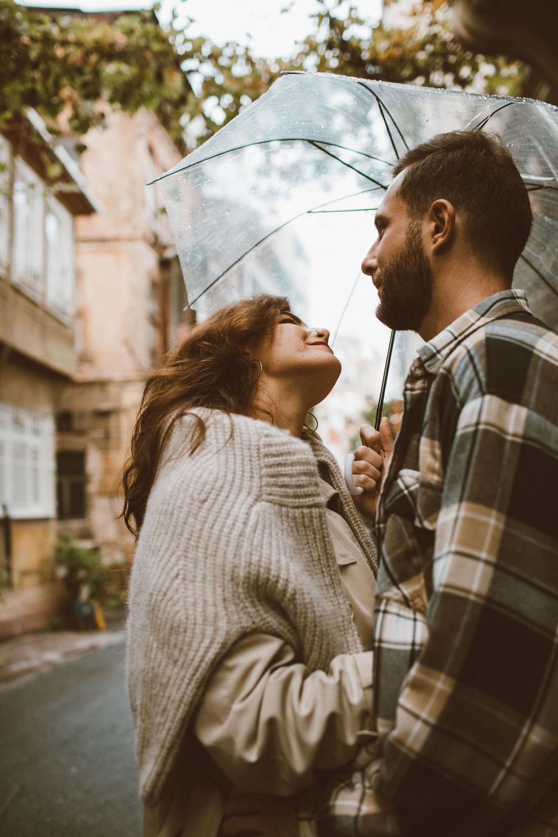 Two people looking at each other under a clear umbrella in the rain